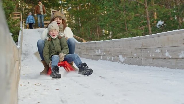 Slow motion of woman and little boy sledding and screaming in delight in winter