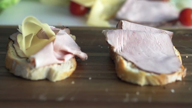 View of cheese falling on sandwich with ham on wooden board, super slow motion 240fps
