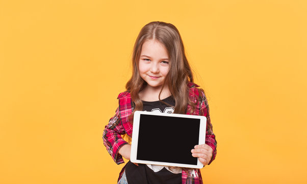 little girl showing blank black tablet pc on yellow background