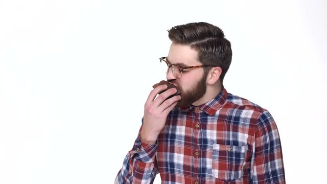 Terrified young bearded man in eyeglasses holding fist near face and staring at you while standing against white background