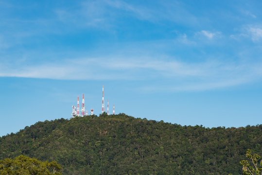Telecommunication towers with TV antennas and satellite dish on the green hill against blue sky with warm light.