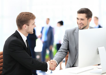 Two happy young men shaking hands while sitting at the office