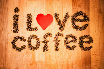 Coffee beans on wood background. Shape of words I Love Coffee made from coffee beans, decorated with red heart on wooden surface. Roasted coffee beans on rustic wood background. Top view. 