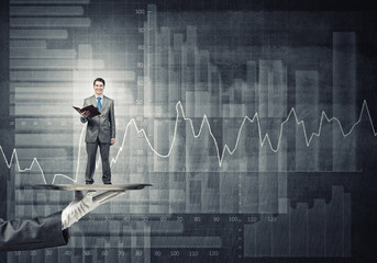 Businessman on metal tray with red book in hands against concrete background with chart