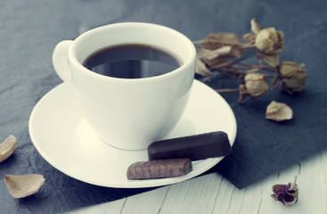Cup of coffee on a saucer, candies and dry roses on a table