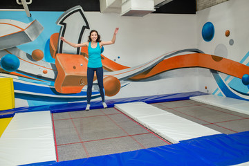 Jumping young woman in trampoline sport center indoors
