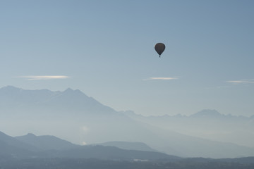 Hot air balloon flying over mountains landscape with winter haze