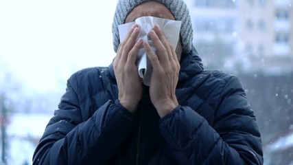 Sick man sneezing and blowing nose in snowy weather in city, super slow motion 240fps
