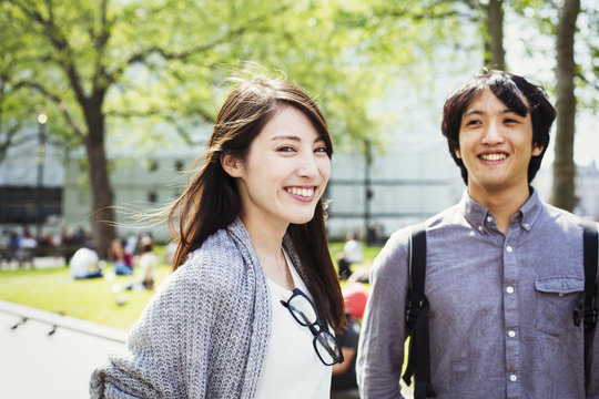 Young Japanese Man And Woman Enjoying A Day Out In London, Standing In A Park, Smiling.