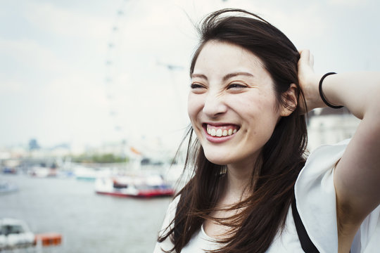 Young Japanese enjoying a day out in London, standing by the River Thames, London Eye in the background.