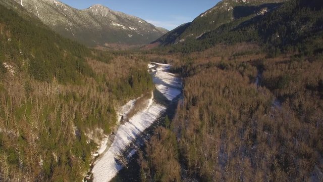 Sunny Day Winter Aerial Flying Up River in Valley of Pacific Northwest Mountain Forest