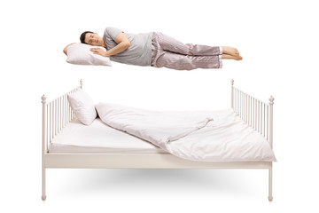 Young man sleeping and floating above a bed