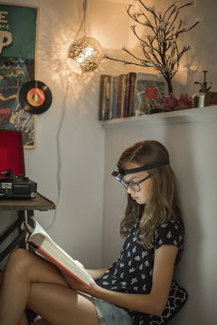 Girl reading book in quiet corner using  head torch