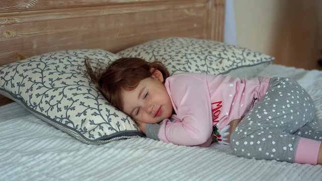 A happy little girl in pajamas lying on bed