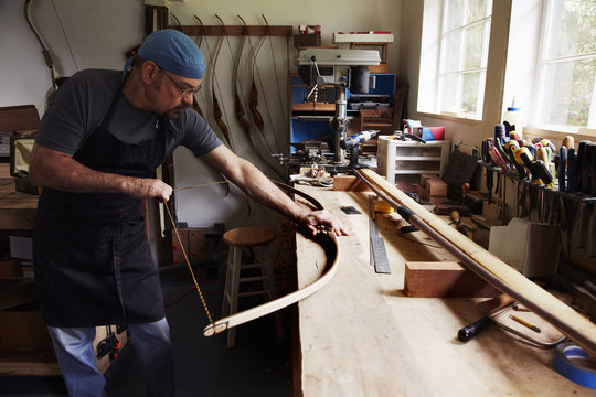 A bowman, a skilled man making a bow, in his workshop. 