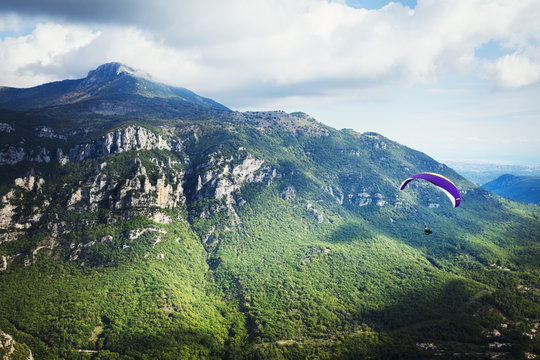 A paraglider in flight over a valley in the mountains. 