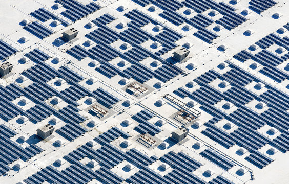 Aerial view of a solar farm, blue photovoltaic solar panels set out in a grid pattern. 