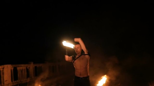 Fire show performance. Three handsome male fire performers dance twirling two fire batons staff ignited from both sides each. Slow motion