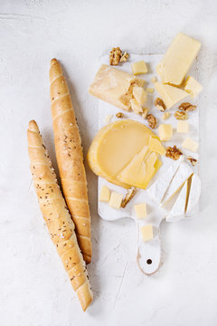 Cheese plate. Assortment of cheese with walnuts and bread on white wood serving board over white concrete texture background. Top view with space.