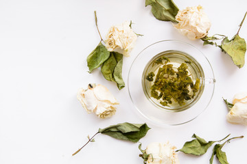 Concept of a cup of green tea with dry white roses around. Square. Isolated. Toned. 