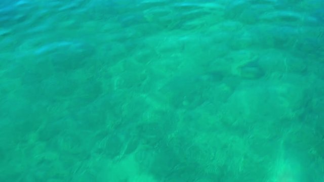 We can see a beautiful light blue and green surface of the sea water. There are small waves on the surface, too. The day is sunny and it is summer time.
