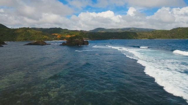 The coast of the tropical island with the mountains and the rainforest on a background of ocean with big waves.Aerial view: sea and the tropical island with rocks and waves. Seascape: sky, clouds