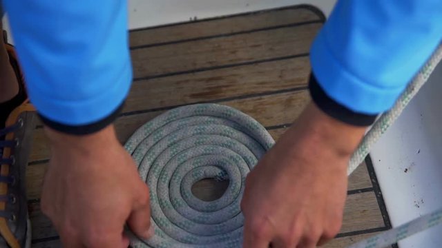 A man is making a circle out of the rope. He is doing this very carefully and folding it into a nice shape. He is sitting on a sailing boat.
