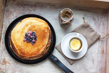 Pancakes, berries, jam and tea on a wooden tray selective focus