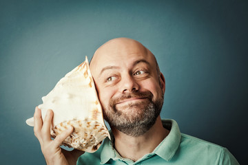 Bearded middle-aged  man with shell listening noise of sea