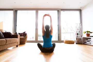 Young woman exercising at home, stretching arms.