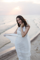 Beautiful young brunette woman in white long dress at the sea shore