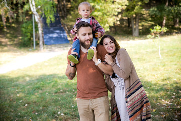 Fototapeta premium Happy joyful young family with child. Father, mother and little boy having fun outdoors in orchard garden, playing together in summer park. Mom, Dad, baby laughing and enjoying nature
