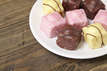 A plate full of fondant fancies cakes on a rustic wooden table top background with blank space at side