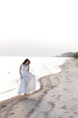 Beautiful young brunette woman in white long dress at the sea shore