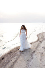Fototapeta na wymiar Beautiful young brunette woman in white long dress at the sea shore