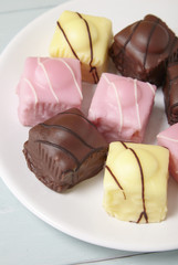 A plate full of fondant fancies cakes on a wooden table top background