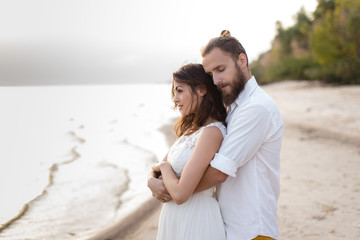 Beach honeymoon couple kissing and hugging on white sand beach. Newlyweds happy in love relaxing on summer holidays. Travel vacation concept.