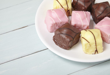 A plate full of fondant fancies cakes on a wooden table top background with empty space at side