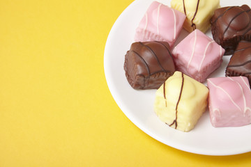 A plate full of fondant fancies cakes on a bright yellow background with blank space at side