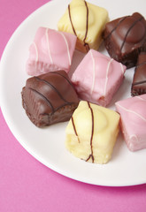 A plate full of fondant fancies cakes on a hot pink background