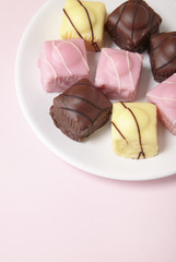 A plate full of fondant fancies cakes on a pastel pink background with empty space below