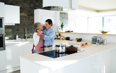 Senior couple in the kitchen cooking and dancing together.