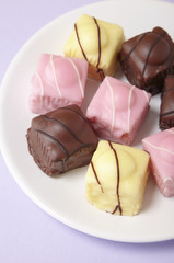 A plate full of fondant fancies cakes on a pastel purple background