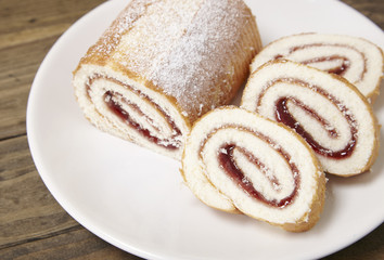 A strawberry jam Swiss roll cake on a rustic wooden table top background