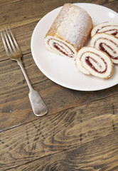 A strawberry jam Swiss roll cake on a rustic wooden table top background with empty space below