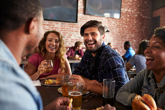 Friends Eating Out In Sports Bar With Screens In Background