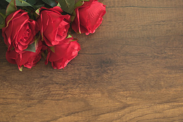 Artificial red roses on wooden table with copy space