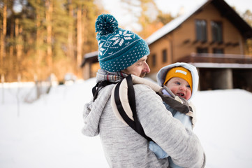 Father holding his son in baby carrier. Sunny winter nature.