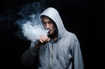 One man in the hood vaping e-cigarette and blowing a cloud.