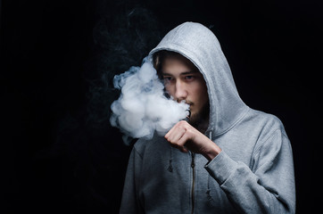 One man in the hood vaping e-cigarette and blowing a cloud.